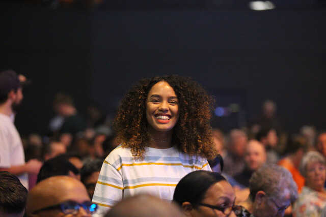 woman standing up in a crowd smiling