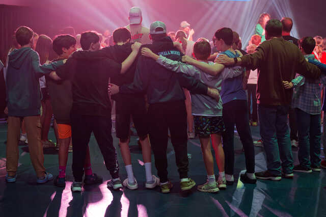 Middle School guys wrap arms around each other in worship